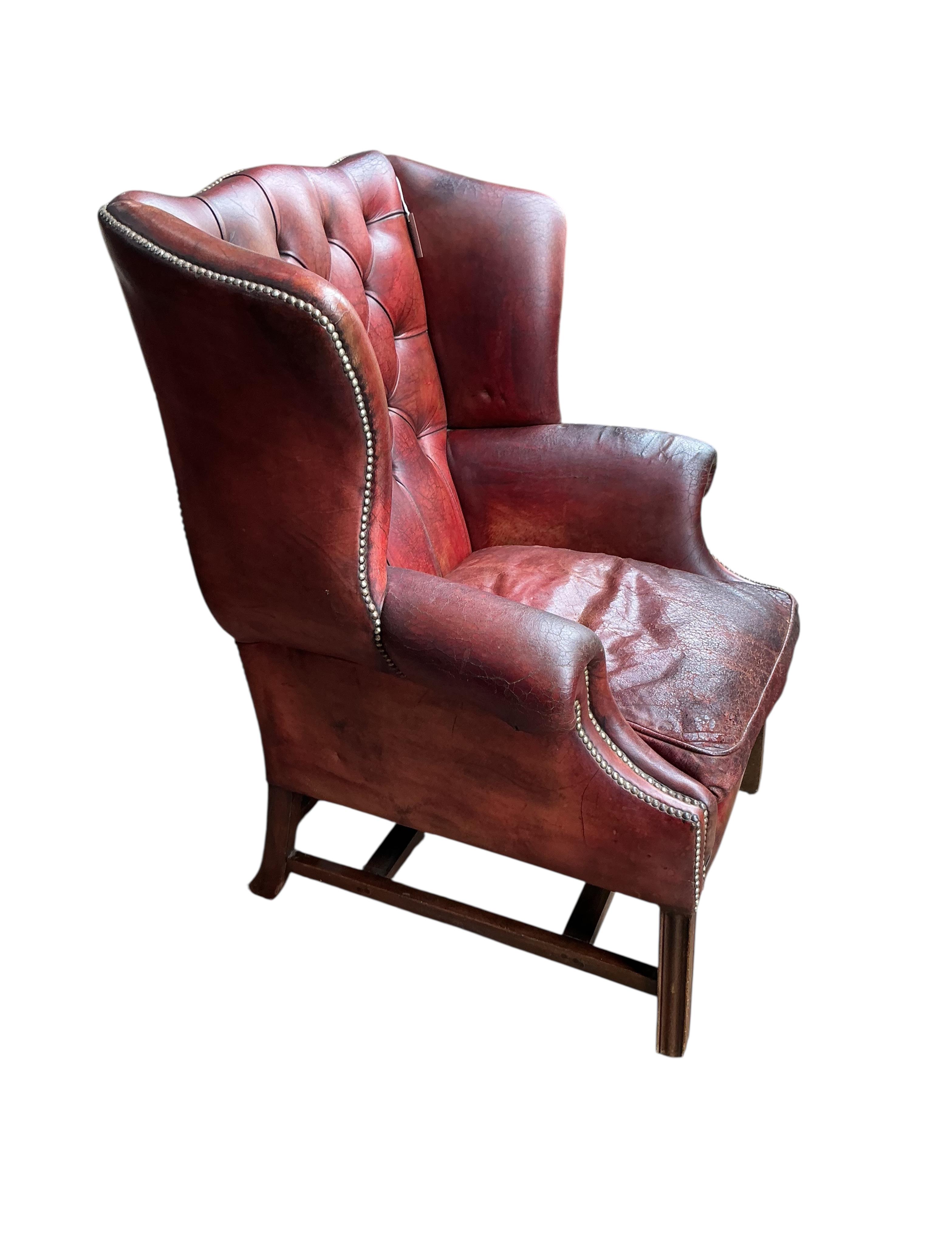 A George III style buttoned burgundy leather wing armchair